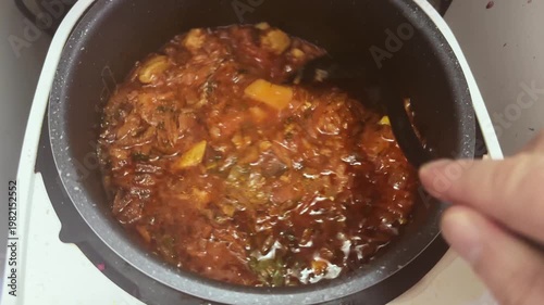 Stirring red borscht with soup ladle in multi-cooker pot