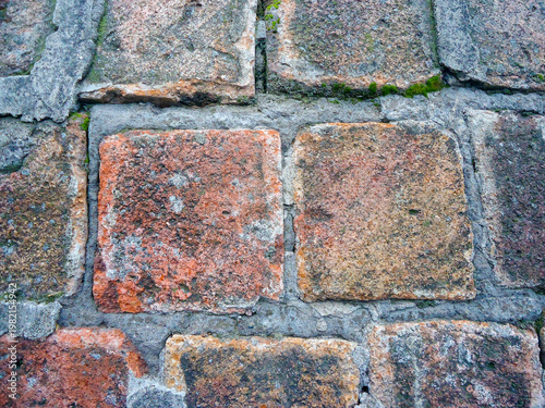 A wall made of about 9 old square bricks of varying shades of brown with jagged edges, held together with grey cement.