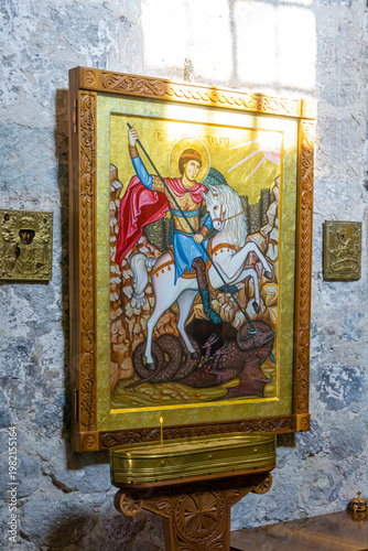 The icon of Saint George on horseback is partially illuminated by sunlight from a window. A candle burns. Saro, Meskheti, Javakheti, Georgia.
