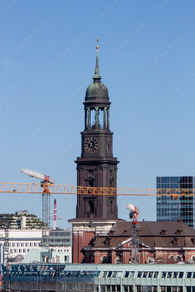 Obraz premium The historic St. Michaelis Church tower, known as Michel, with construction cranes in the foreground under a blue sky in Hamburg