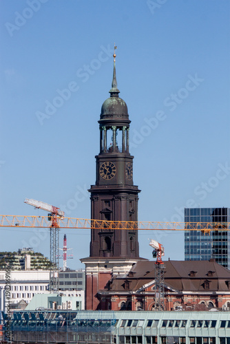The historic St. Michaelis Church tower, known as Michel, with construction cranes in the foreground under a blue sky in Hamburg