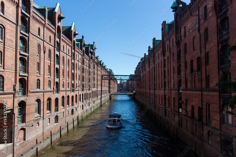 Naklejka premium Tourist boat sailing on a canal in the historic Speicherstadt district with red brick warehouse buildings in Hamburg, Germany