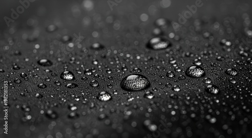 Raindrops rest upon a dark textured waterproof fabric surface.