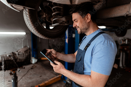 Mechanic checks car repair using tablet in workshop during the day