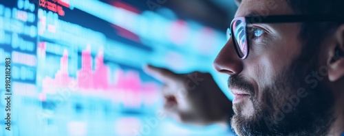 Side view of a bearded man in glasses, intensely analyzing glowing blue financial charts on a large screen, his finger highlighting market data for strategic insight. Digital, Trading