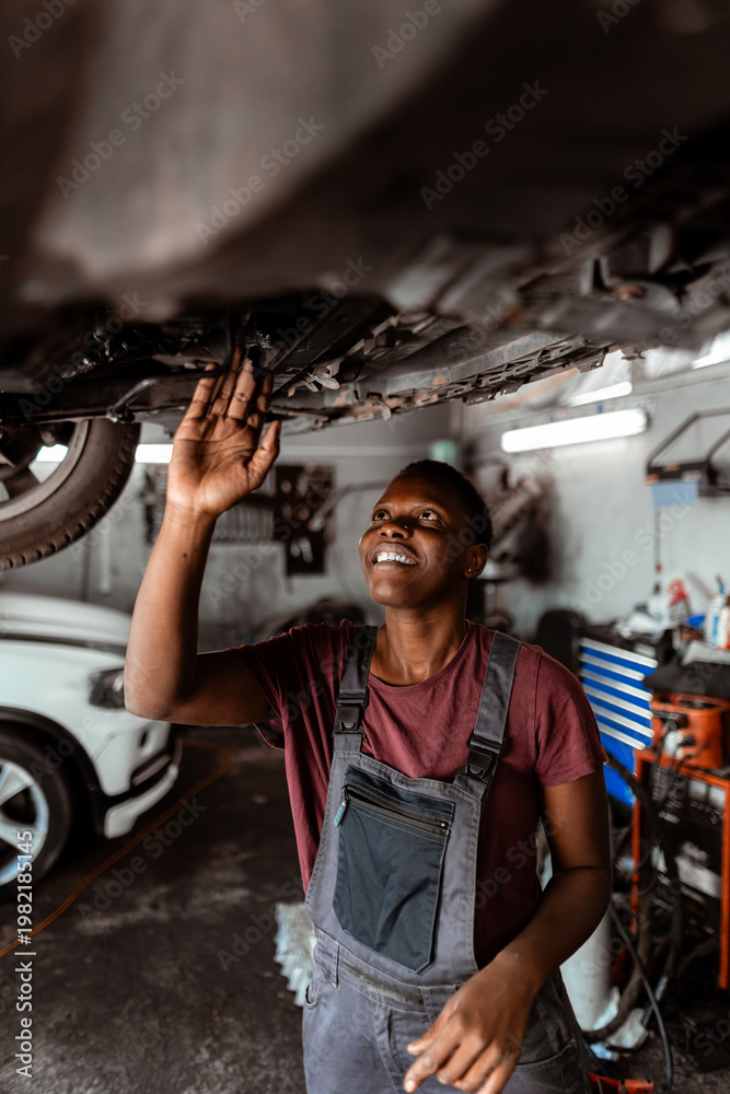 Obraz premium Worker repairs car under vehicle in garage during daytime in busy auto shop
