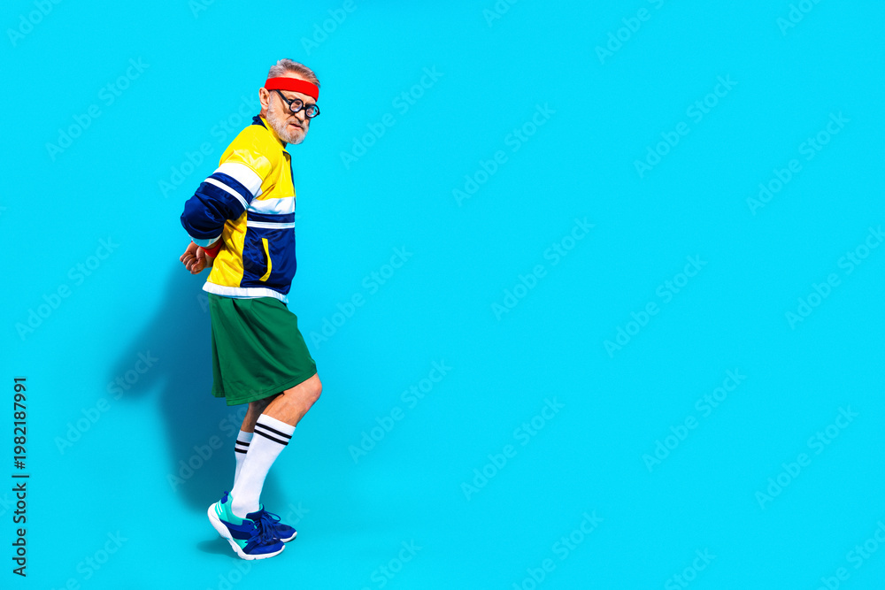 Obraz premium Elderly man in retro sportswear posing confidently for senior fitness and active lifestyle portrait on bright blue background
