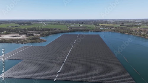 Wide aerial orbit of floating solar farm with sunlight reflection on water