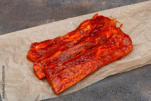 Frisch marinierte Schweinebauchscheiben in Paprikamarinade auf Backpapier.