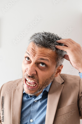 Angry mature businessman scratching head looking up in frustration