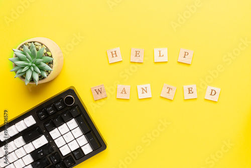 Creative flat lay composition with keyboard, succulent flower and text Help Wanted on bright yellow background.Hiring and recruitment of office staff concept.