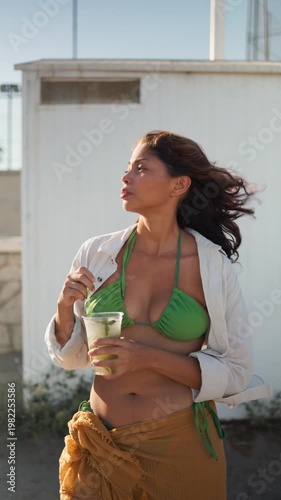 Young happy woman drinking a fresh mojito cocktail on a sandy beach during a summer sunset