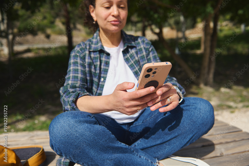 Fototapeta premium Woman sitting cross-legged outdoors using smartphone in sunny park