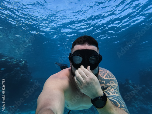 Athletic tattooed man free diving in the crystal clear blue waters of the Red Sea exploring coral reef ecosystems