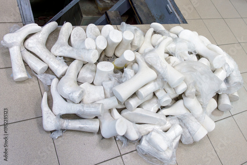 Orthopedic shoe production materials including multiple white shoe lasts arranged on a tiled floor, showcasing various shapes and sizes for footwear design and fitting