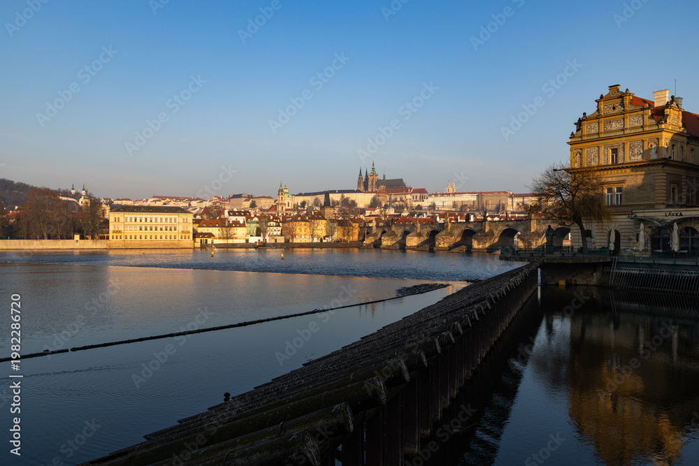 Obraz premium scenic view of Prague Castle and Charles Bridge glowing in golden light over the Vltava River