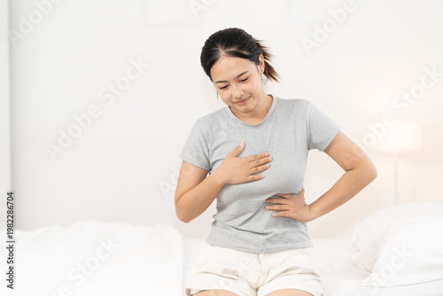 Young Asian woman performing breast self examination, checking for lumps and early signs of breast cancer at home, healthcare awareness, prevention and female medical screening concept breast.