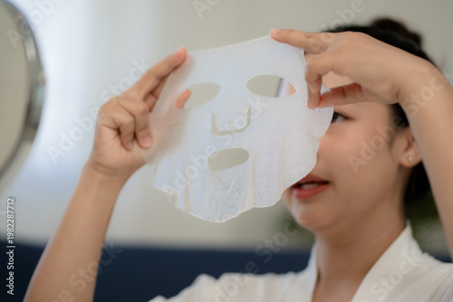 Young Asian woman holding facial sheet mask before applying on face, skincare preparation step, beauty routine concept, self care, cosmetic treatment and healthy glowing skin lifestyle