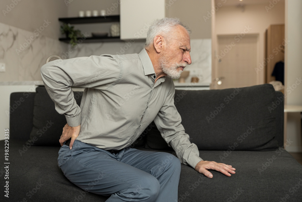 Fototapeta premium Elderly man feeling severe back pain, sitting on a sofa
