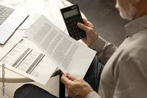 Man reviews utility bills and balances finances with calculator at home office
