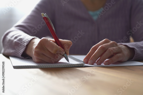 Close up of woman writing in paper notebook with pen
