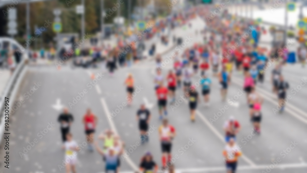Obraz premium Blurry urban street scene with many runners moving forward. Diverse participants in athletic wear show effort and focus. Spectators line the road, adding community energy