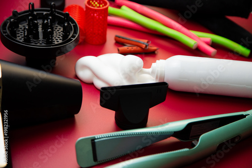 Close-up side view on a pink background, hairdryer with attachments, stylers and curling irons for straightening and creating curls, foam for volume and long-lasting, curlers in different shapes and