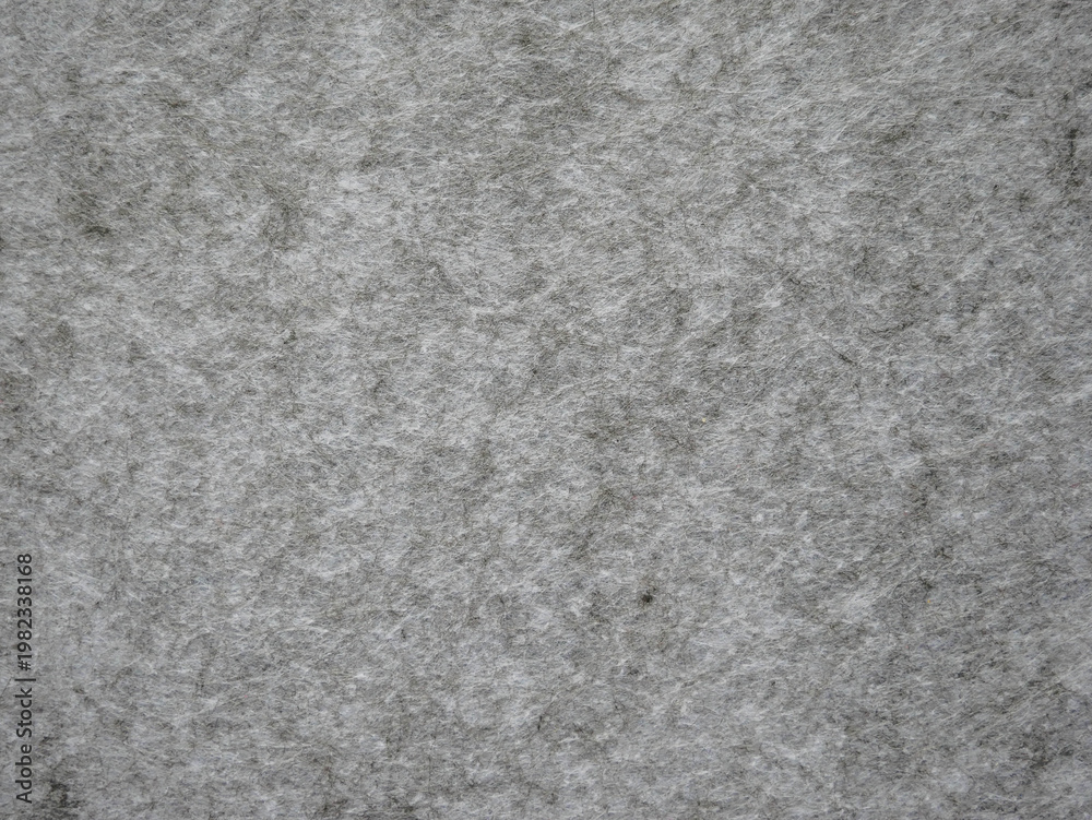 Fototapeta premium Macro close-up of a light gray melange felt fabric sheet with visible fibrous texture and subtle dark fiber flecks. The mottled, heathered surface gives a natural, organic quality ideal for neutral te