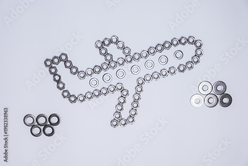 An artistic composition made of nuts, washers, and bolts forming an airplane flying among the clouds. The central structure is elongated and symmetrical, with wings. 