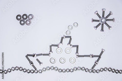 An artistic composition made of nuts, washers, and bolts forming a ship sailing on the sea. The central structure is elongated and symmetrical. To the right appears a sun made of metal pieces, 