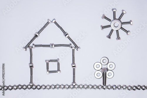 An artistic composition made with screws, nuts, and washers on a white background. The metal pieces are arranged to form a house with a triangular roof, a window in the center