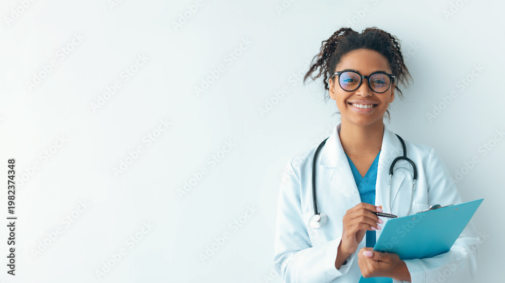© Prostock-studio - A young female doctor stands by a white wall in an office. She smiles while holding a clipboard. She wears a white coat and has glasses on. Her stethoscope hangs around her neck. © Prostock-studio - A young female doctor stands by a white wall in an office. She smiles while holding a clipboard. She wears a white coat and has glasses on. Her stethoscope hangs around her neck.