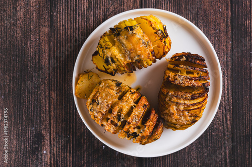 Close up of baked Hasselback potatoes with cheese, garlic and herbs on a plate on the table top view