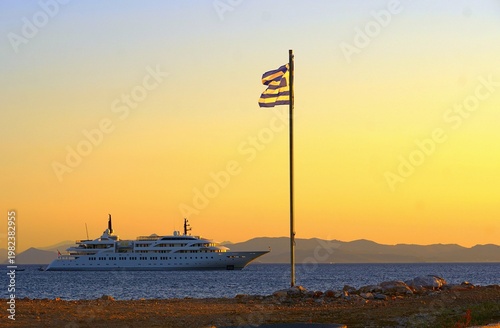 A superyacht and a Greek flag, at sunset, from the coast of Glyfada, Greece