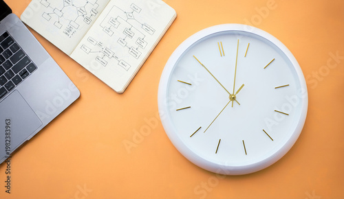 Business planning and time management concept with laptop, notebook with flowchart and clock on orange background