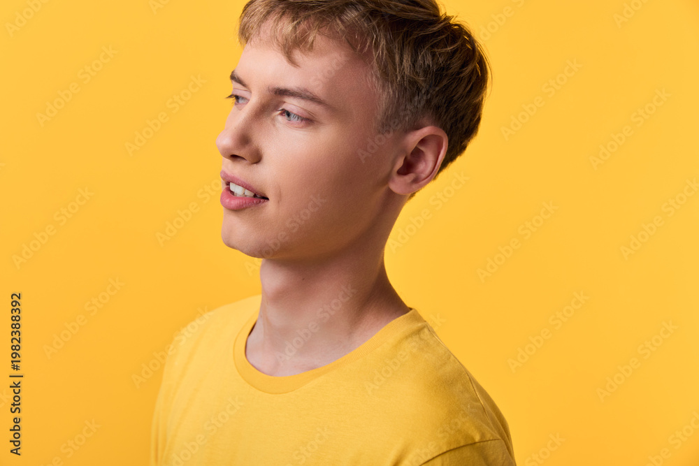 Fototapeta premium Young man in a yellow shirt stands against a bright yellow background with studio lighting, creating a casual style and warm mood ideal for lifestyle, fashion or wellness campaigns