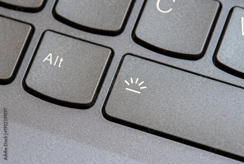 Macro close-up of a modern laptop keyboard backlight control key with illumination symbol next to Alt button, black notebook computer keys in angled view, technology shortcut detail, no people
