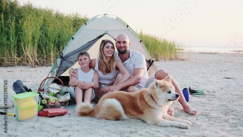 Happy family sitting in the tent on the beach with Akita Inu