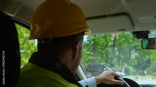 Man in construction helmet driving car and holding steering wheel with his hands. Male foreman in hard hat on the way to the construction site. Real time video