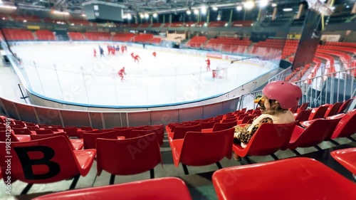 Little girl watching ice hockey training in indoor arena stands