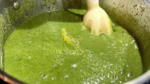 close up of metal pot of green mixed vegetable broth with blender moving around