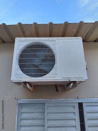Outdoor Air Conditioner Unit Mounted on Wall Under Roof Close Up HVAC System Cooling Equipment Exterior Building Maintenance Concept