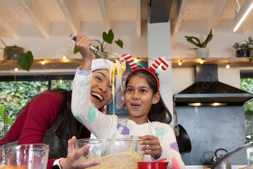 Asian mother and child whisking batter at countertop with mixing bowl, in Santa hat and headband