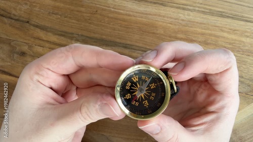 Female Caucasian hand holding and showing a small kids compass with cord, demonstrating navigation tool up close. 4K video on wooden table background.
