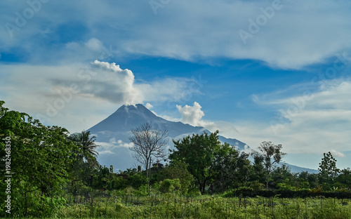 Merapi volcano small eruption at crater with cloudy blue sky background