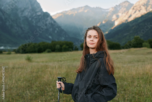 A thoughtful hiker woman stands outdoors in rugged landscape, holding trekking poles. She wears a lightweight jacket and gazes ahead, conveying calmness, exploration, and adventure.