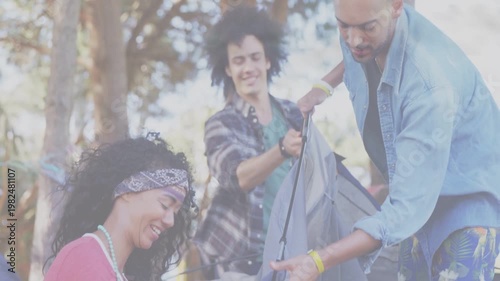 Three friends unfolding gray tent in park, coordinating poles and clips while preparing campsite