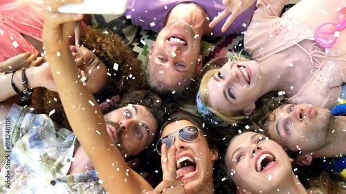 Friends lying heads together raising smartphone posing playfully as confetti falls for social media