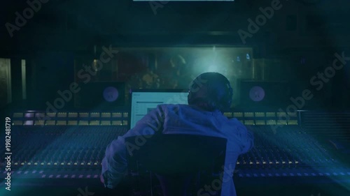 Male audio engineer getting live take cue, tweaking faders, watching animated meters, raising arms