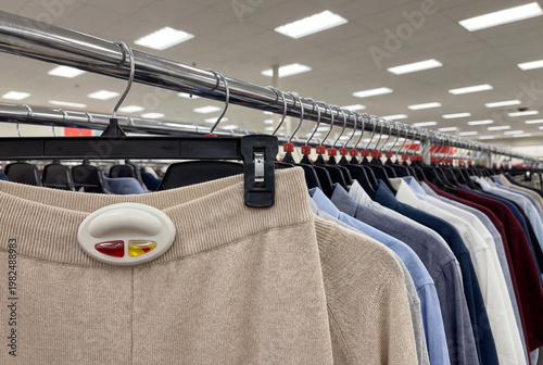 Anti-theft security tag attached to beige knit pants on a clothing rack